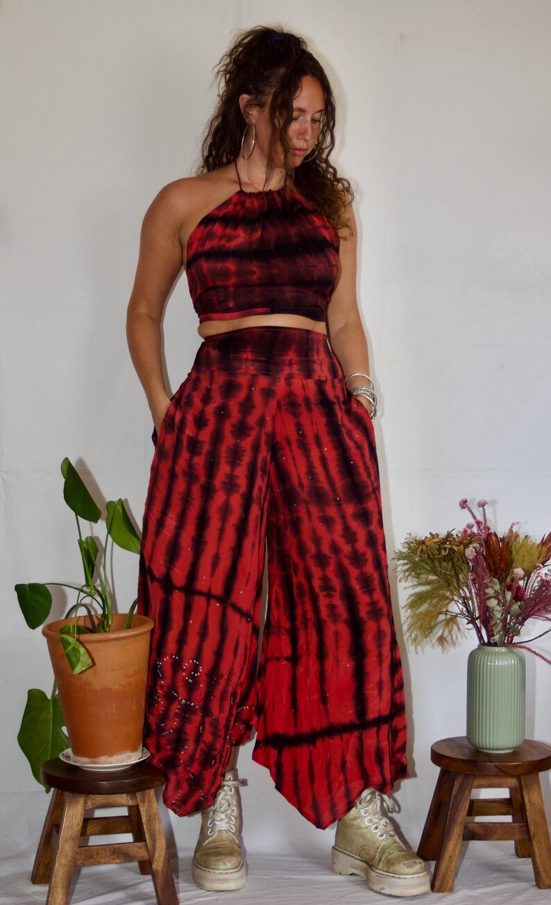 May include: A two-piece tie-dye outfit in red and black. The halter top and wide-leg pants have a vertical stripe pattern. The pants have pockets and are embellished with small, scattered beads. The outfit is paired with platform boots.