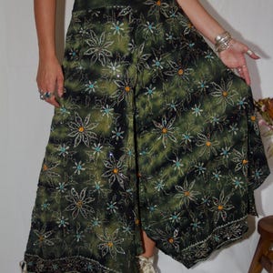 May include: Green and black palazzo pants with a floral pattern. The pants have a wide leg design and are embellished with sequins. The fabric has a tie-dye effect. The pants are part of a set with a matching crop top.