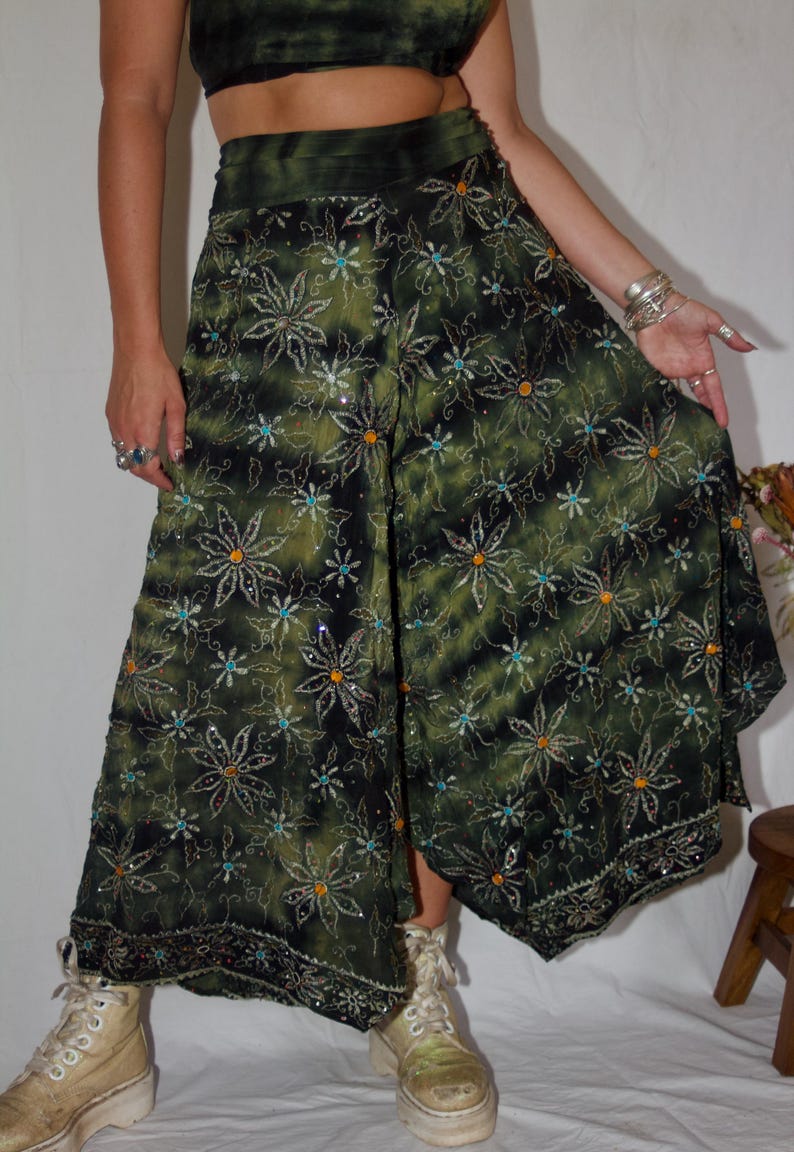 May include: Green and black palazzo pants with a floral pattern. The pants have a wide leg design and are embellished with sequins. The fabric has a tie-dye effect. The pants are part of a set with a matching crop top.