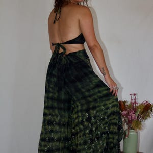 May include: A two-piece outfit featuring a halter top and wide-leg pants. The top and pants are a dark green tie-dye pattern. The pants have a floral pattern near the hem. The outfit is paired with platform shoes.