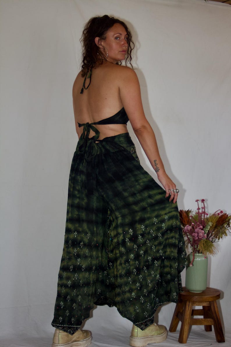 May include: A two-piece outfit featuring a halter top and wide-leg pants. The top and pants are a dark green tie-dye pattern. The pants have a floral pattern near the hem. The outfit is paired with platform shoes.