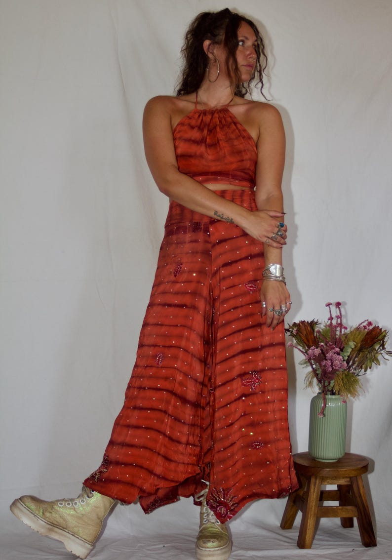 May include: A two-piece orange halter top and wide-leg pants set with a striped pattern and embellished details. The outfit is paired with platform boots. The ensemble is a bohemian style.