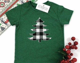 May include: A green t-shirt featuring a black and white buffalo plaid Christmas tree design. The shirt has short sleeves and a tag that reads "ICE CREAM LIFE". Red berries and a festive patterned ribbon are also visible.