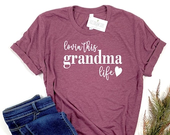 May include: A maroon t-shirt with the text "lovin' this grandma life" in white with a white heart.