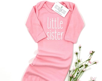 May include: Pink baby gown with long sleeves and a white inscription that reads "little sister".