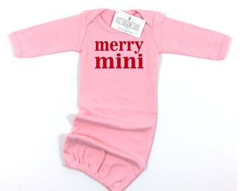 May include: A light pink baby gown with long sleeves and the words "merry mini" printed in red. The gown has a tag that reads "ICE CREAM LIFE". The gown is designed for newborns.