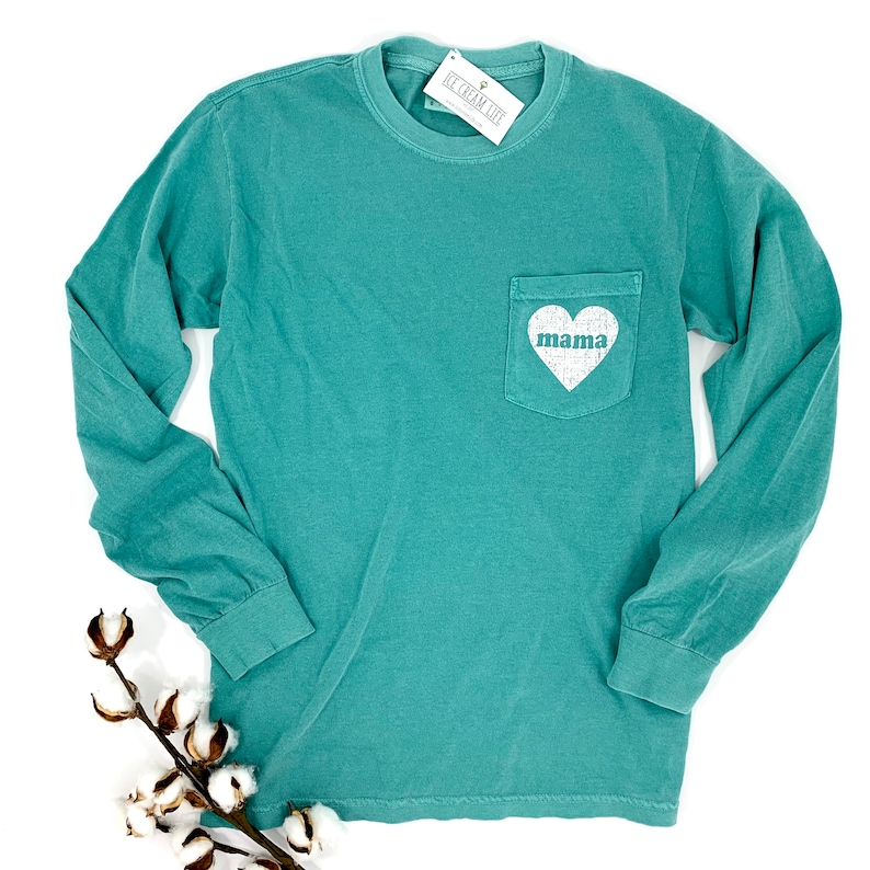 May include: Teal long-sleeve t-shirt with a white pocket and the word "mama" inside a white heart.