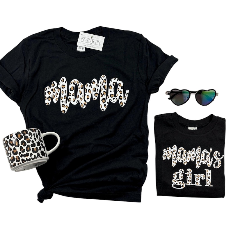 Pode incluir: Duas camisetas pretas com um design de estampa de leopardo. A camiseta maior diz "mama" e a camiseta menor diz "mama's girl".