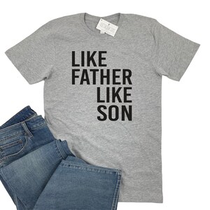 May include: A gray t-shirt with the text "Like Father Like Son" printed in black.