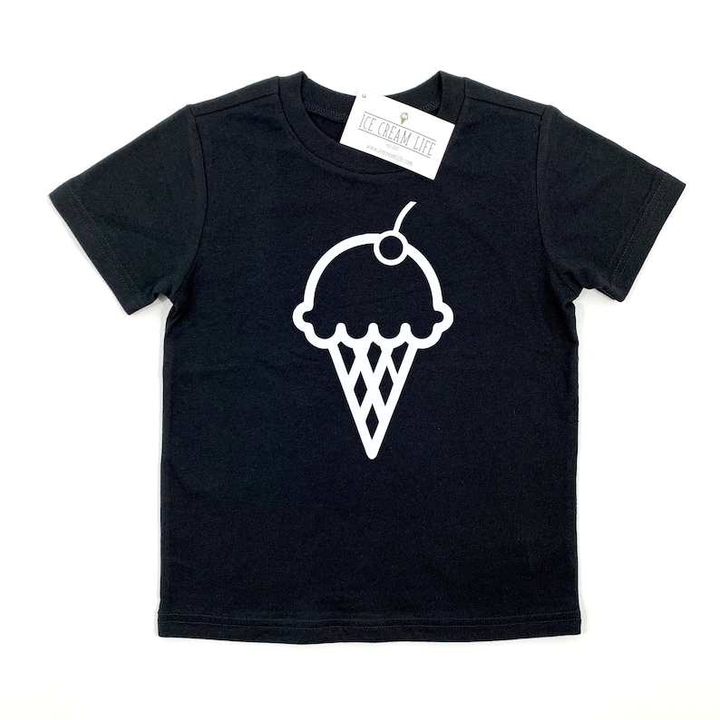 Peut inclure: T-shirt &agrave; manches courtes noire avec un graphique de cornet de glace blanc. Le cornet de glace a une cerise sur le dessus. Le t-shirt a le texte "ICE CREAM LIFE" sur une &eacute;tiquette.