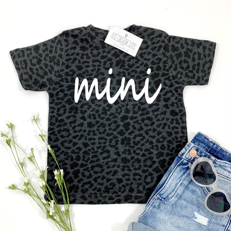 May include: A black and grey leopard print t-shirt with the word "mini" in white text.