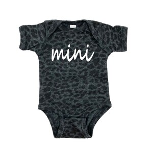 May include: A black and gray bodysuit with a leopard print pattern. The bodysuit has short sleeves and a white inscription that says "mini".