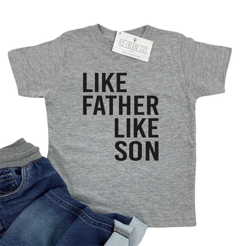 May include: A heather grey t-shirt with the text "Like Father Like Son" printed in black.