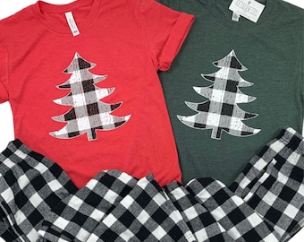 May include: Two short-sleeved t-shirts, one red and one green, each with a plaid Christmas tree design. Black and white plaid pajama pants are visible below the shirts. The shirts have a tag that says "Ice Cream Life".