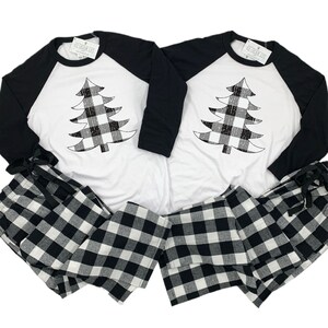 K&ouml;nnte beinhalten: Passendes Pyjama-Set in Schwarz-Wei&szlig;-Karos mit einem wei&szlig;en Langarmshirt mit einem schwarzen und wei&szlig;en karierten Weihnachtsbaum-Design. Das Shirt hat schwarze Raglan&auml;rmel.
