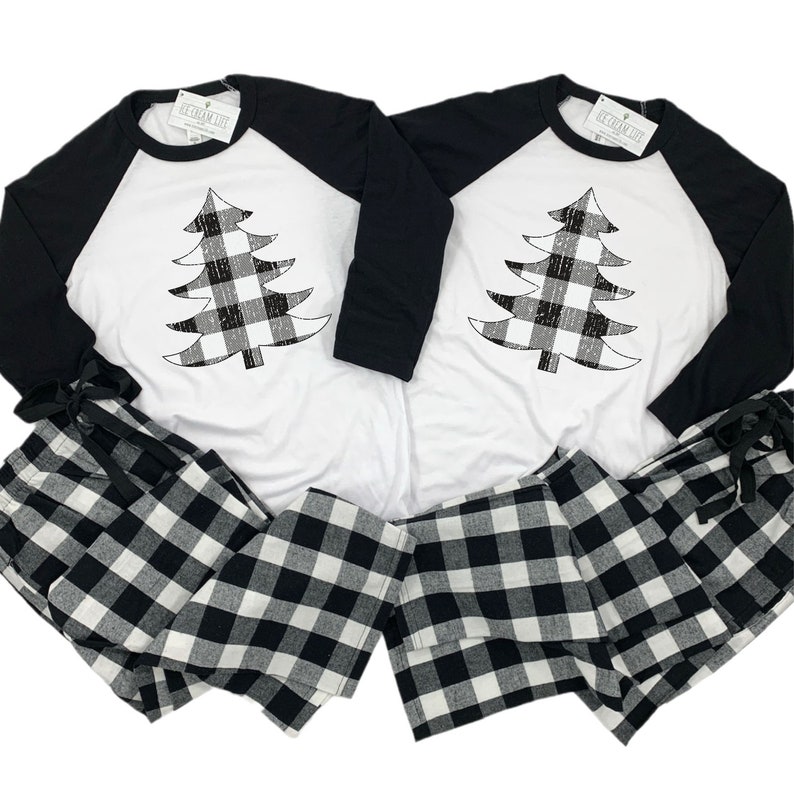 K&ouml;nnte beinhalten: Passendes Pyjama-Set in Schwarz-Wei&szlig;-Karos mit einem wei&szlig;en Langarmshirt mit einem schwarzen und wei&szlig;en karierten Weihnachtsbaum-Design. Das Shirt hat schwarze Raglan&auml;rmel.