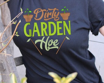 Può includere: Maglietta nera con testo verde che recita "Dirty Garden Hoe" con due piccole piante in vaso e due zappe da giardino marroni su entrambi i lati del testo.