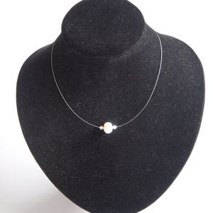 May include: A simple necklace with a single white pearl pendant on a clear string.