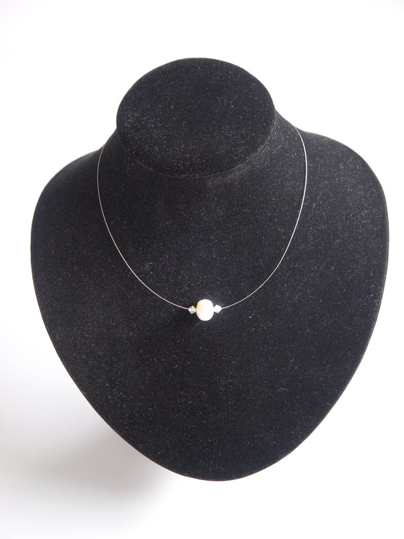 May include: A simple necklace with a single white pearl pendant on a clear string.