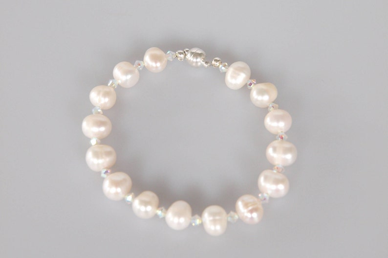 May include: A white pearl bracelet with a silver clasp. The bracelet is made with small white pearls and clear crystals.