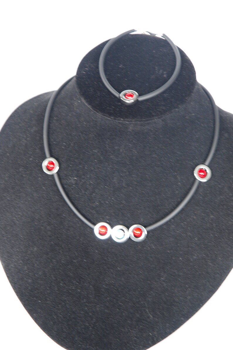 May include: A black necklace with red and silver beads on a black velvet display stand.