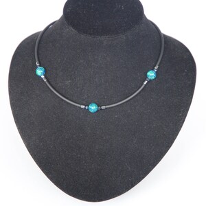 May include: A black choker necklace with three turquoise blue beads. The necklace is displayed on a black velvet mannequin bust.