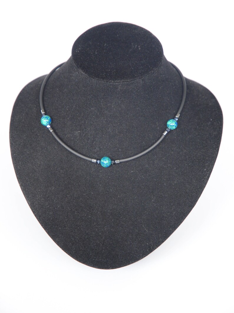 May include: A black choker necklace with three turquoise blue beads. The necklace is displayed on a black velvet mannequin bust.