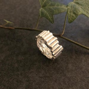 Peut inclure: Une bague en argent avec un design texturé et strié. La bague est en métal et a un look unique et moderne.