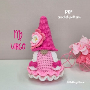 May include: A crochet doll featuring a tall pink pointed hat adorned with a layered pink and white flower. The doll has a pink dress with white ruffled trim, white braided hair, and small pink bows. Text reads: PDF crochet pattern, Virgo, and LittleMagicHouse.