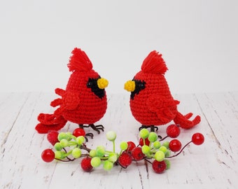 Op de afbeelding: Twee rode gehaakte kardinaalvogels met zwarte ogen en gele snavels zitten op een tak met rode bessen en groene bladeren.