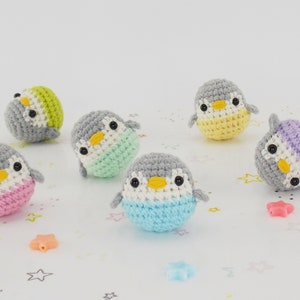 Op de afbeelding: Zes kleine gehaakte pinguïn speelgoedjes in verschillende kleuren, waaronder roze, blauw, groen, geel en paars. De pinguïns kijken allemaal naar voren met hun ogen dicht.