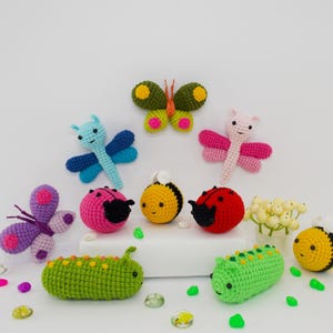 Könnte beinhalten: Eine Sammlung gehäkelter Insektenspielzeuge, darunter ein Schmetterling, ein Marienkäfer, eine Biene, eine Libelle und eine Raupe. Die Spielzeuge sind in verschiedenen Farben hergestellt, darunter Pink, Blau, Grün, Gelb und Rot.
