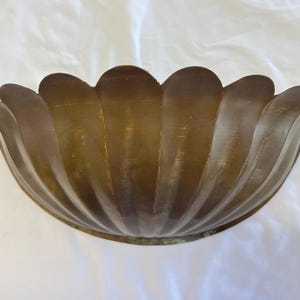 May include: A vintage, bronze-colored metal bowl with a scalloped rim. The bowl has a rounded, petal-like design and a smooth, reflective surface. The bowl is likely used for decorative purposes.