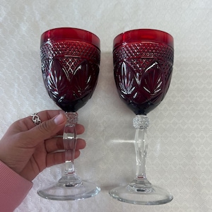 May include: Two red wine glasses with a clear glass stem and base. The glasses have a diamond pattern and a floral design.