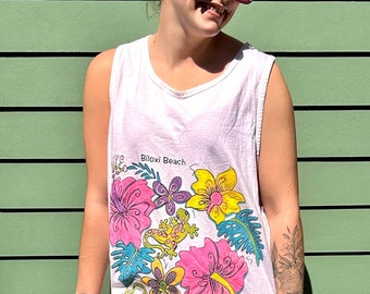 Pode incluir: Vestido branco maxi sem mangas com estampa floral e o texto "Biloxi Beach". O vestido tem uma fenda lateral e apresenta flores, folhas e lagartos coloridos.