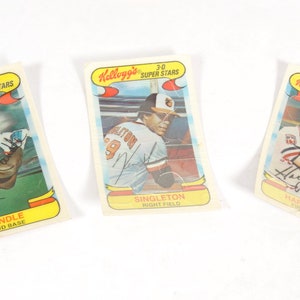 May include: Three vintage Kellogg's Super Stars baseball cards featuring photos of baseball players with their names and positions printed below. The cards are in good condition with slight wear and tear.