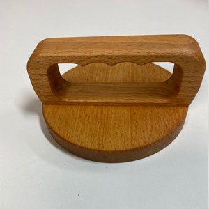 May include: A wooden lid with a handle. The handle has a cutout design and is made of light brown wood. The lid is round and has a smooth surface.