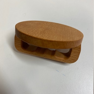 May include: A wooden hair clip with a rounded top and a carved design. The clip is light brown in color.