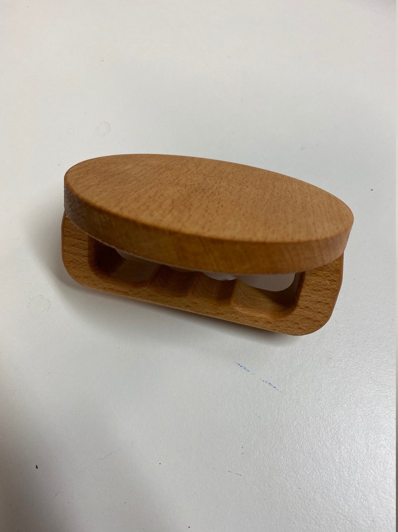 May include: A wooden hair clip with a rounded top and a carved design. The clip is light brown in color.