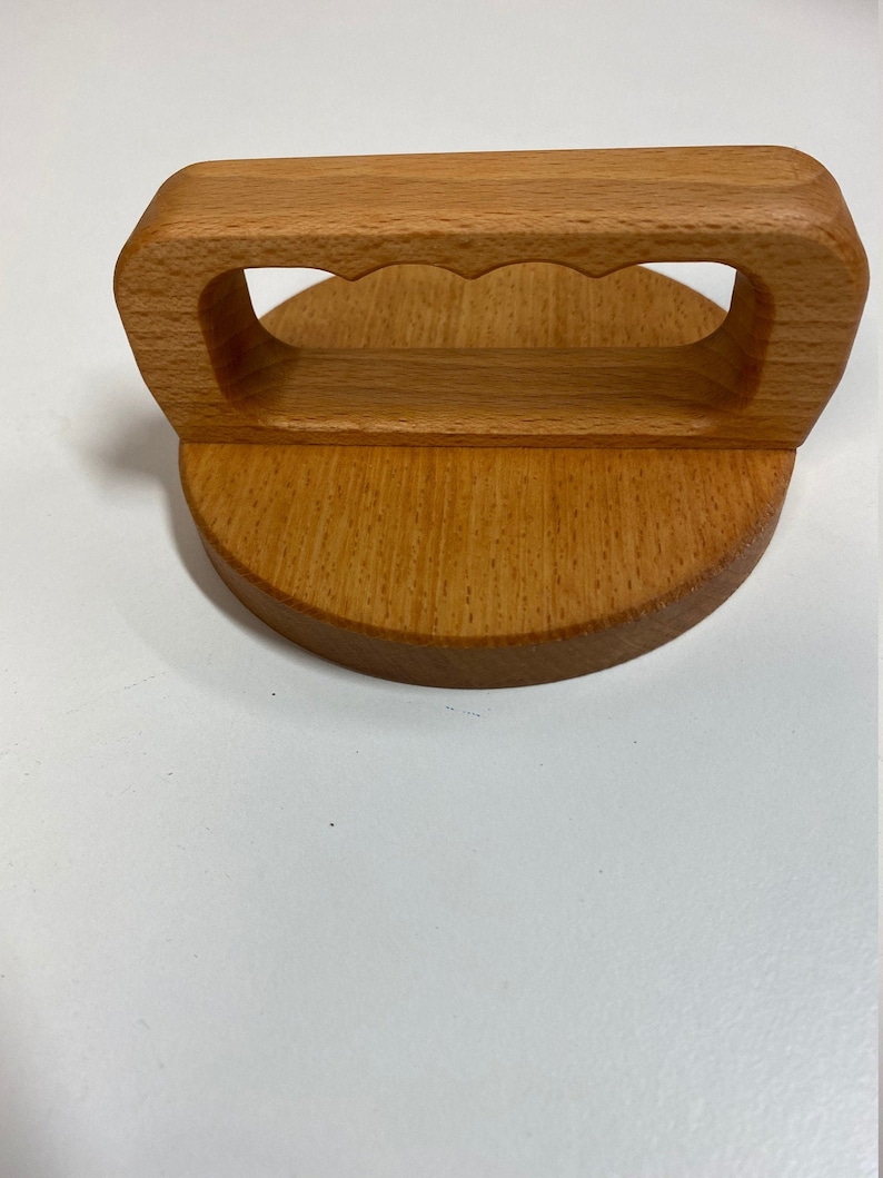 May include: A wooden lid with a handle. The handle has a cutout design and is made of light brown wood. The lid is round and has a smooth surface.