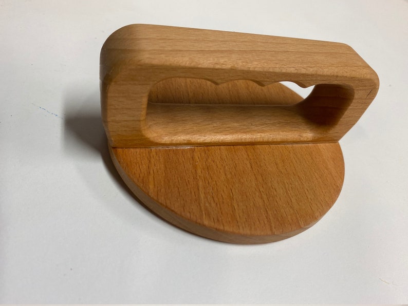 May include: A wooden kitchen tool with a round base and a handle with a cutout. The tool is made of light brown wood.