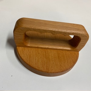 May include: A wooden lid with a handle. The handle has a unique design with three cutouts. The lid is made of light brown wood.