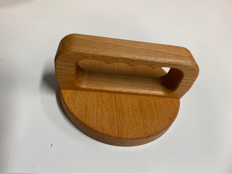 May include: A wooden lid with a handle. The handle has a unique design with three cutouts. The lid is made of light brown wood.