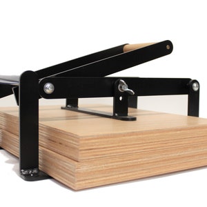 May include: A black metal press with a wooden handle, used for pressing together multiple pieces of plywood.