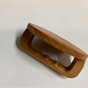 May include: A wooden clamp with a rounded top and a cutout handle. The clamp is made of light brown wood and has a natural finish.