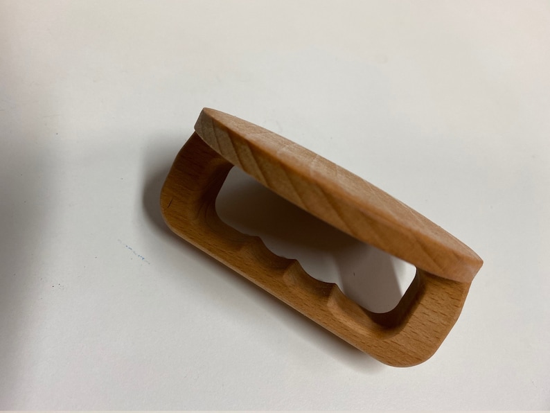May include: A wooden clamp with a rounded top and a cutout handle. The clamp is made of light brown wood and has a natural finish.