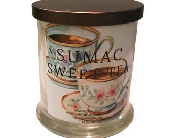 May include: A clear glass candle jar with a dark brown lid. The jar features a label with the text "SUMAC SWEET TEA" and a watercolor illustration of teacups with floral designs. The candle is a natural soy candle.