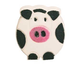 May include: A wooden button in the shape of a pig. The button is off-white with black spots and a pink snout. The pig has two small black eyes and two small black feet.