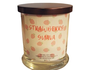 May include: A clear glass jar candle with a bronze lid. The label reads "STRAWBERRY GUAVA" with strawberry illustrations. The candle is 12 fl oz and made with natural soy wax.