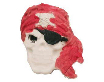 May include: A skull-shaped decorative item with a red bandana and a black eye patch. The bandana has a white skull and crossbones emblem. The skull is white with a detailed facial structure, perfect for Halloween or pirate-themed decor.